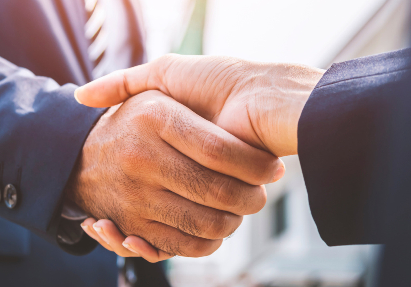 Handshake between two people in business suits, outdoor setting.